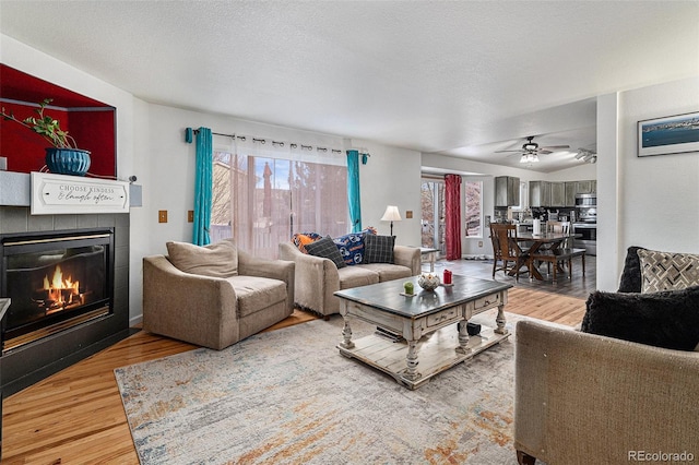 living room with a tiled fireplace, a textured ceiling, ceiling fan, and hardwood / wood-style flooring