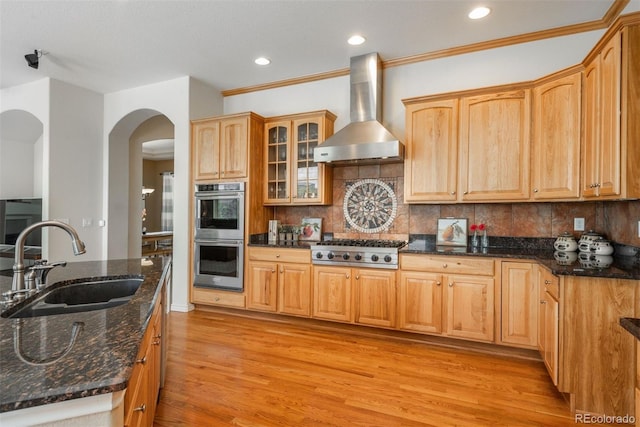 2105 Baguette Dr, Castle Rock, CO 80108 - kitchen featuring wall chimney range hood, stainless steel appliances, light wood finished floors, arched walkways, and dark stone counters