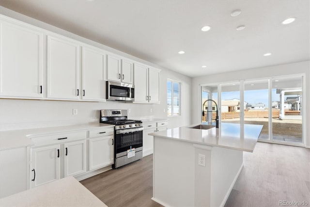 kitchen with sink, white cabinetry, a kitchen island with sink, stainless steel appliances, and light hardwood / wood-style floors