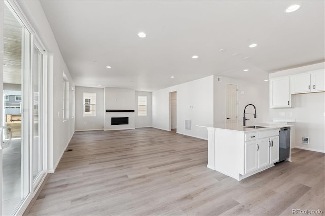 kitchen featuring white cabinetry, sink, an island with sink, and light wood-type flooring