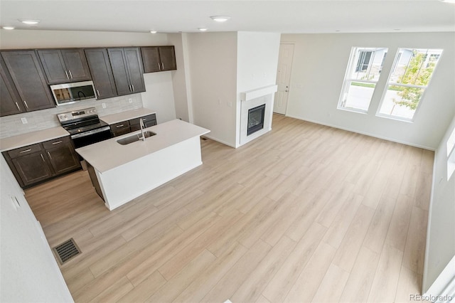 13568 E 111th Ave, Commerce City, CO 80022 - kitchen featuring appliances with stainless steel finishes, decorative backsplash, light wood finished floors, light countertops, and a kitchen island with sink