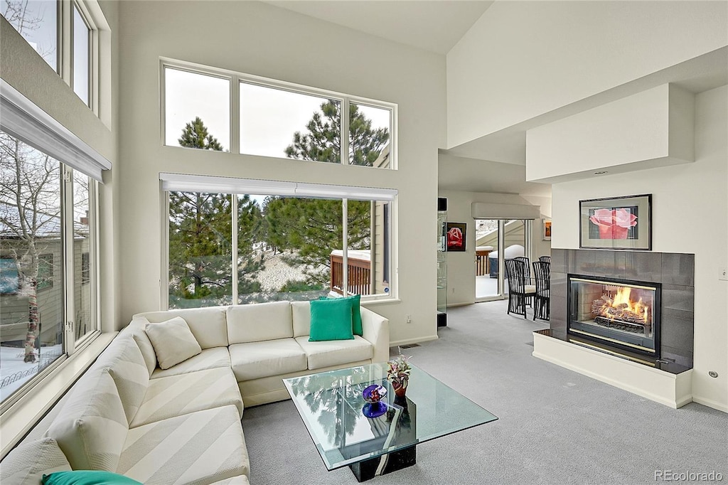 living room featuring a tiled fireplace, carpet floors, and a towering ceiling