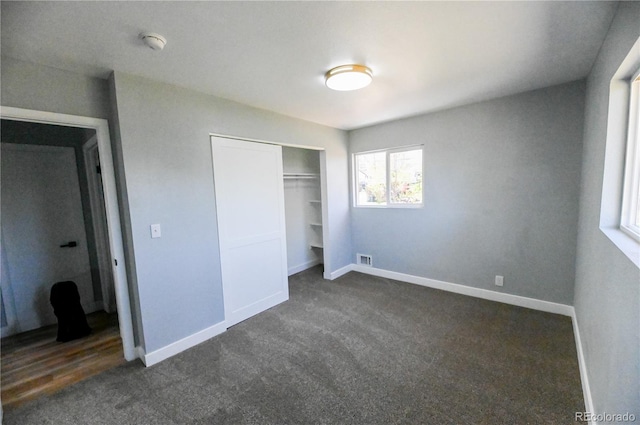 unfurnished bedroom featuring dark colored carpet, a closet, baseboards, and visible vents