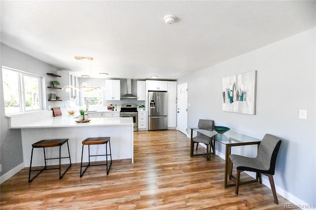 kitchen featuring a sink, a peninsula, stainless steel appliances, wall chimney range hood, and white cabinetry