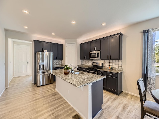 917 White Leaf Cir, Castle Rock, CO 80108 - kitchen featuring appliances with stainless steel finishes, a sink, light stone countertops, light wood-type flooring, and a kitchen island with sink