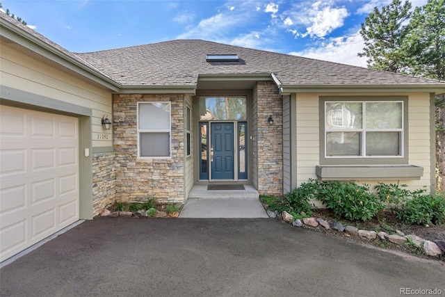 property entrance featuring a shingled roof, stone siding, an attached garage, and aphalt driveway