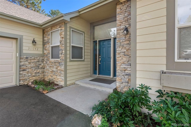 entrance to property with a garage, stone siding, and a shingled roof