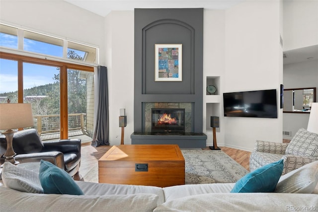 living room with visible vents, a towering ceiling, a glass covered fireplace, light wood-type flooring, and baseboards