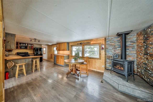 dining space with sink, hardwood / wood-style flooring, a wood stove, rail lighting, and wood walls