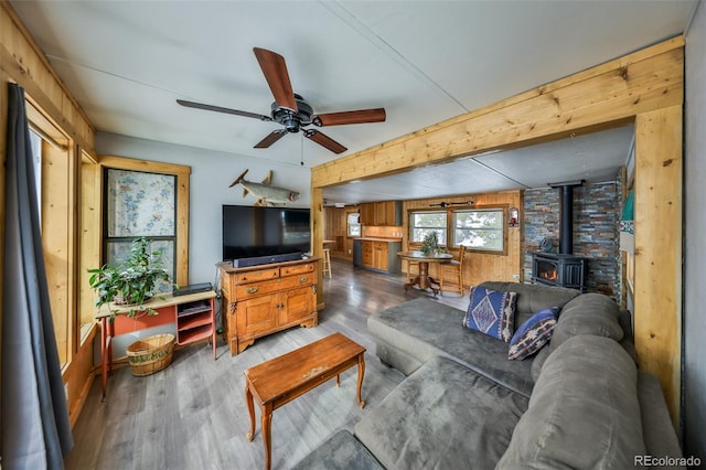 living room featuring a wood stove, ceiling fan, beam ceiling, wood-type flooring, and wood walls