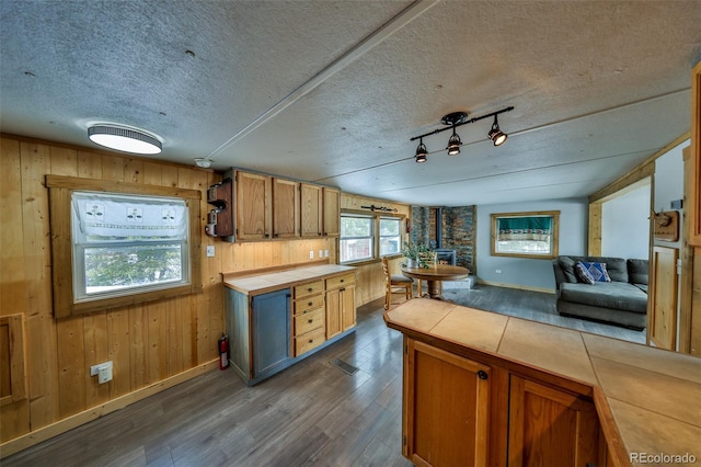 kitchen featuring dark wood-type flooring, wooden walls, tile counters, a textured ceiling, and a wood stove