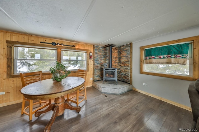 dining space featuring hardwood / wood-style flooring, a wood stove, a textured ceiling, and wood walls