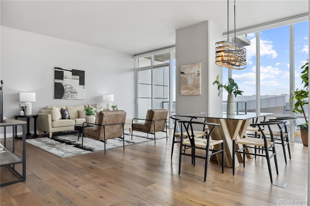 dining room with a healthy amount of sunlight, wood-type flooring, an inviting chandelier, and floor to ceiling windows