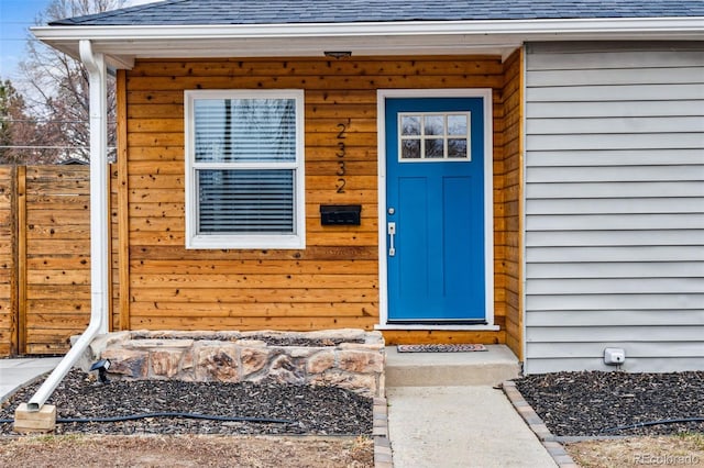 entrance to property featuring a shingled roof and fence