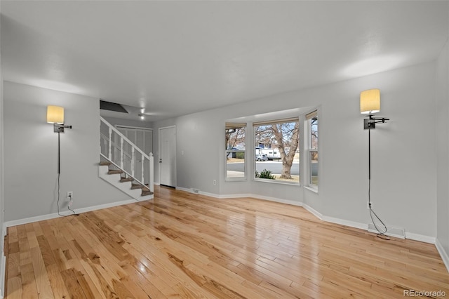 unfurnished living room featuring baseboards, stairs, and hardwood / wood-style flooring