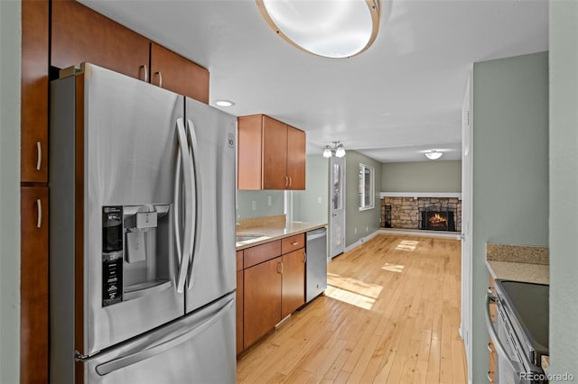 kitchen featuring brown cabinets, stainless steel appliances, light wood-style floors, a stone fireplace, and light countertops