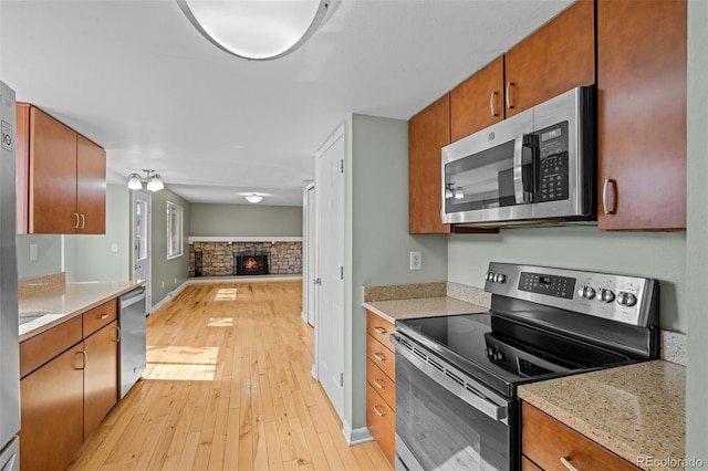 kitchen featuring brown cabinets, a stone fireplace, light wood-style floors, appliances with stainless steel finishes, and open floor plan