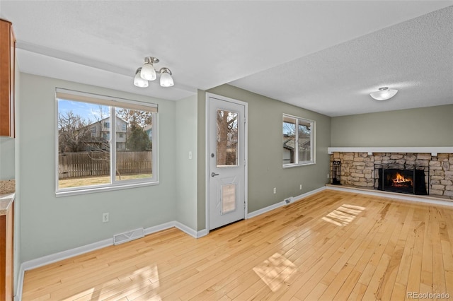 unfurnished living room featuring visible vents, baseboards, hardwood / wood-style floors, a stone fireplace, and a textured ceiling