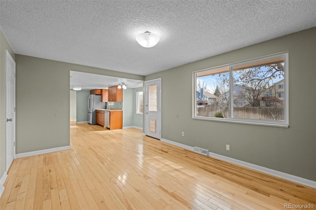 unfurnished living room featuring baseboards, visible vents, light wood finished floors, and a textured ceiling