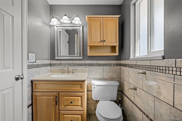 bathroom featuring vanity, tile walls, toilet, and wainscoting