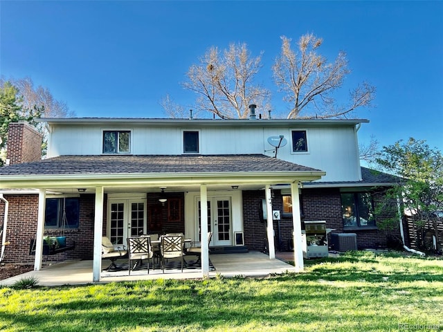 back of property with cooling unit, french doors, brick siding, a patio area, and a lawn