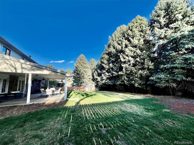 view of yard featuring fence, a storage unit, an outdoor structure, and a patio area