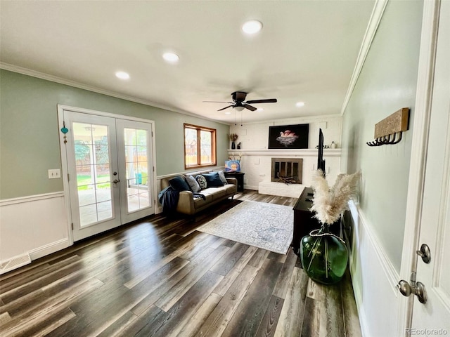 living area featuring french doors, crown molding, wainscoting, a brick fireplace, and recessed lighting
