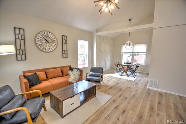 living room featuring plenty of natural light, light wood-type flooring, lofted ceiling, and an inviting chandelier