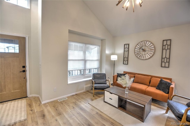 living room featuring a wealth of natural light, high vaulted ceiling, light hardwood / wood-style floors, and an inviting chandelier