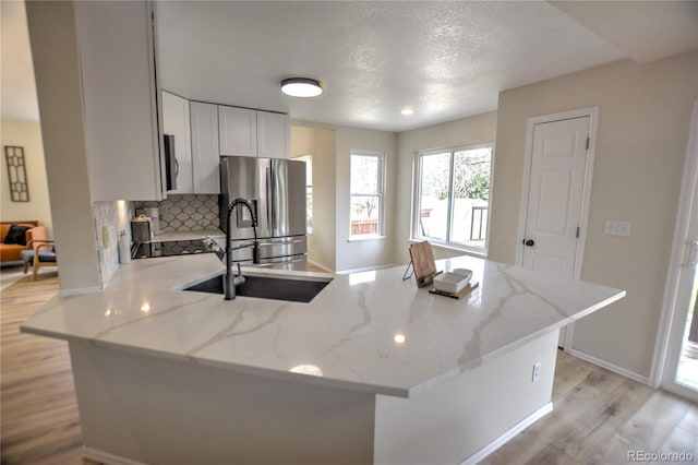 kitchen with light stone countertops, backsplash, stainless steel appliances, sink, and light hardwood / wood-style flooring