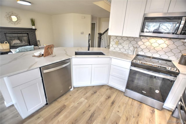 kitchen with white cabinets, sink, a brick fireplace, light hardwood / wood-style flooring, and appliances with stainless steel finishes