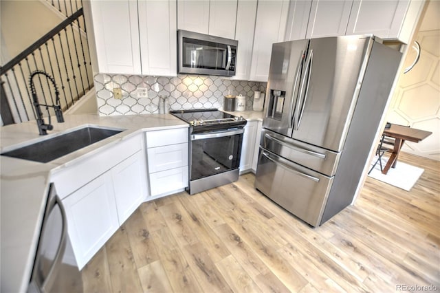 kitchen with white cabinetry, sink, light hardwood / wood-style flooring, backsplash, and appliances with stainless steel finishes