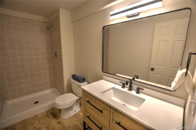 bathroom with tiled shower, hardwood / wood-style floors, vanity, and toilet