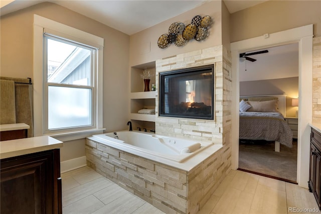 bathroom with tiled tub, vanity, and ceiling fan