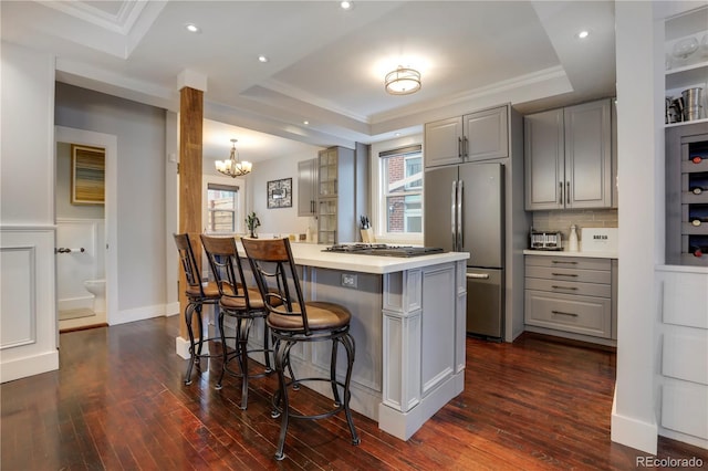 kitchen with gray cabinets, a kitchen breakfast bar, stainless steel appliances, a raised ceiling, and kitchen peninsula