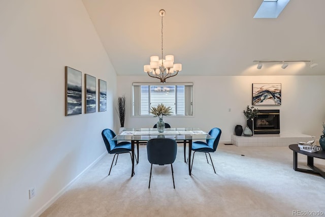 carpeted dining area featuring rail lighting, a chandelier, a tile fireplace, and vaulted ceiling