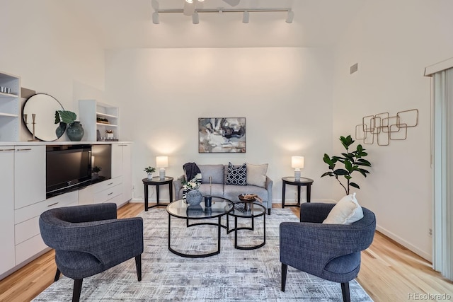 living room with a high ceiling, light hardwood / wood-style floors, and rail lighting