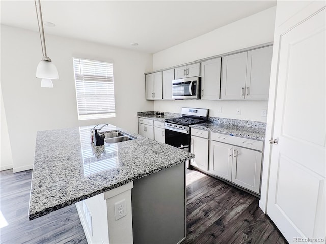 kitchen featuring dark wood-type flooring, a center island with sink, decorative light fixtures, sink, and appliances with stainless steel finishes