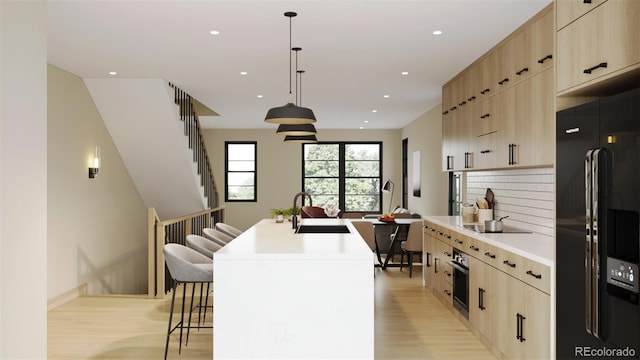 kitchen featuring a breakfast bar, sink, hanging light fixtures, an island with sink, and black appliances