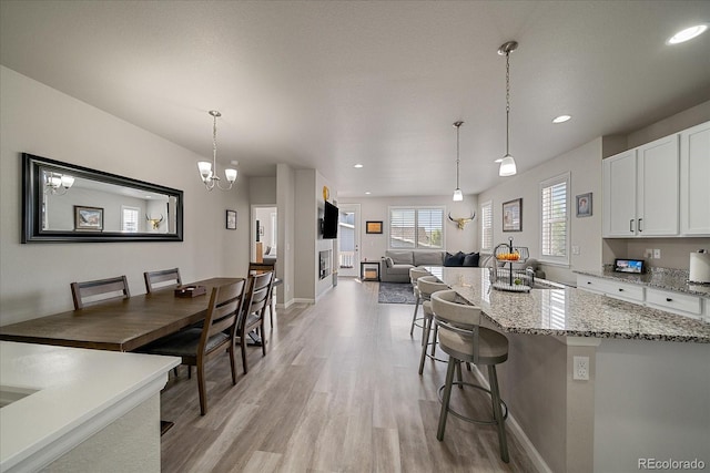 8908 Birch Run Ln, Parker, CO 80134 - kitchen featuring light wood finished floors, white cabinets, light stone countertops, a breakfast bar area, and pendant lighting