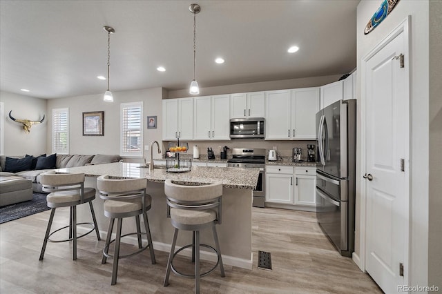 8908 Birch Run Ln, Parker, CO 80134 - kitchen featuring appliances with stainless steel finishes, open floor plan, white cabinets, light stone countertops, and a kitchen breakfast bar