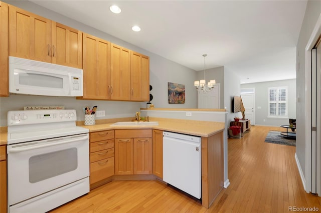 kitchen featuring light countertops, light wood-style floors, a sink, white appliances, and a peninsula