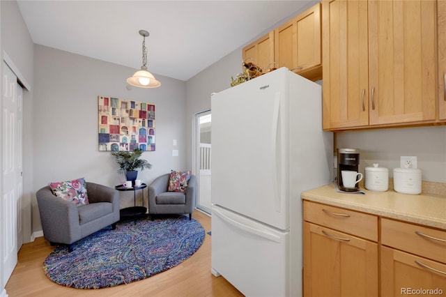 kitchen featuring light wood-style floors, hanging light fixtures, light countertops, freestanding refrigerator, and light brown cabinetry