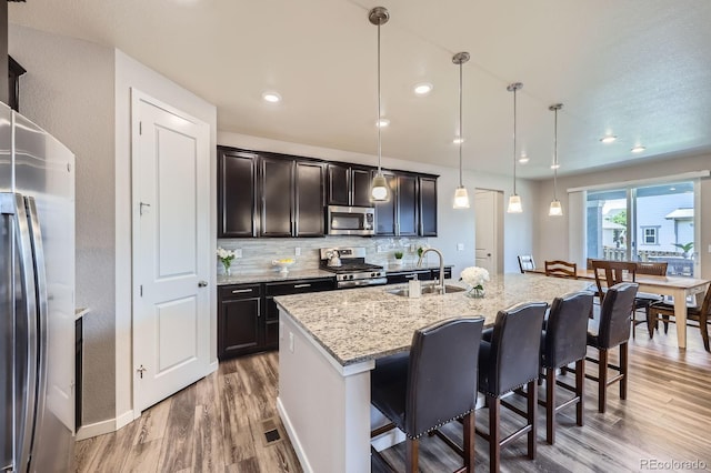 10991 Xanadu St, Commerce City, CO 80022 - kitchen with stainless steel appliances, light wood-style floors, a breakfast bar, light stone counters, and pendant lighting