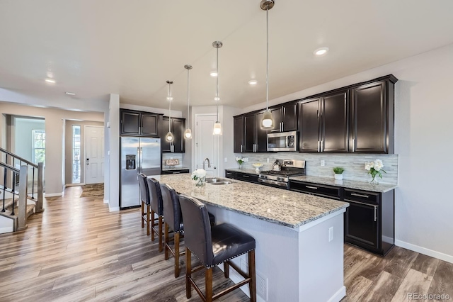 10991 Xanadu St, Commerce City, CO 80022 - kitchen with appliances with stainless steel finishes, light wood-style flooring, a kitchen bar, backsplash, and light stone countertops