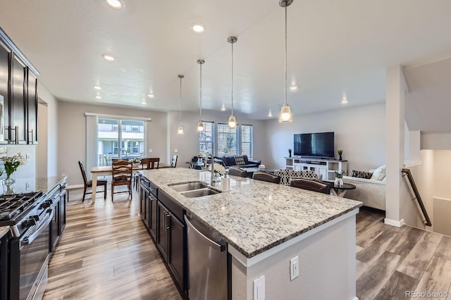 10991 Xanadu St, Commerce City, CO 80022 - kitchen featuring stainless steel appliances, open floor plan, light wood-style flooring, decorative light fixtures, and a center island with sink