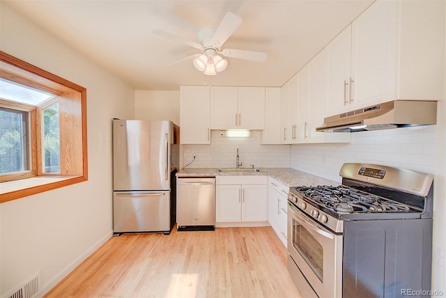 6054 Iris Way, Arvada, CO 80004 - kitchen with stainless steel appliances, under cabinet range hood, light wood finished floors, backsplash, and white cabinets