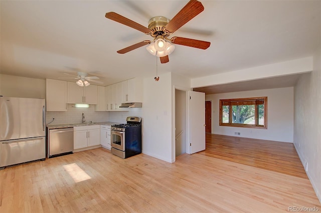6054 Iris Way, Arvada, CO 80004 - kitchen with stainless steel appliances, under cabinet range hood, white cabinetry, light wood-style flooring, and decorative backsplash