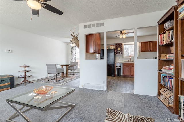 unfurnished living room with ceiling fan, sink, a textured ceiling, and dark colored carpet