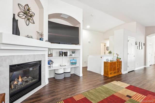 living room with arched walkways, a fireplace, wood finished floors, baseboards, and lofted ceiling